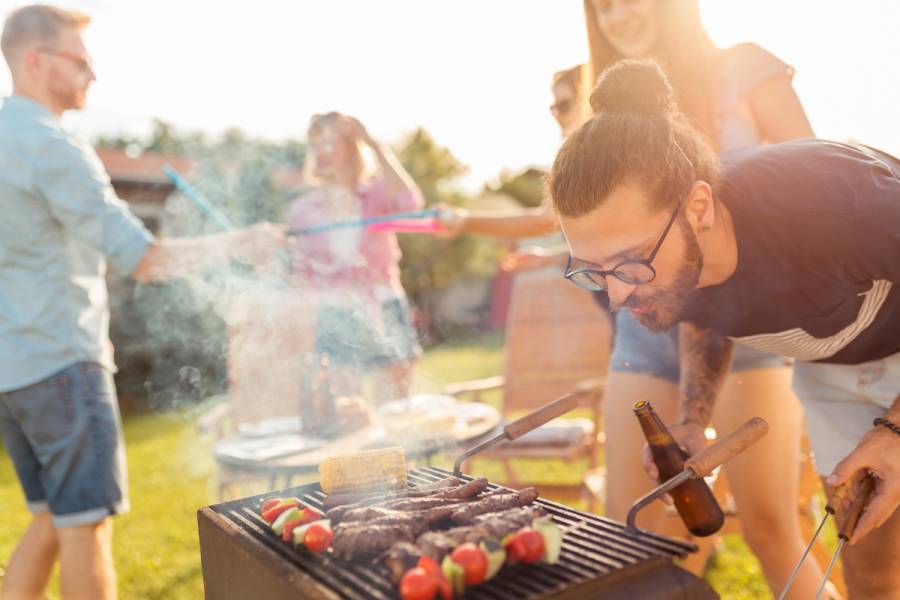 Group of friends having a backyard barbecue party, grilling meat, drinking beer, playing badminton and having fun on a sunny summer day