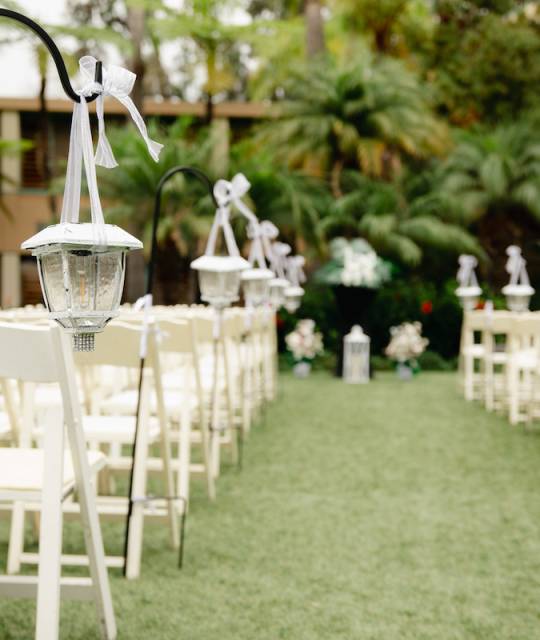 Cloudy tropical wedding venue - ceremony set up with white wooden trees, palm trees and vintage lanterns